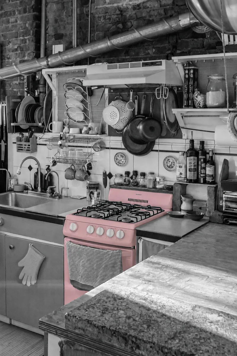 A dusty-pink cooker among well-used pots and pans, with the surrounding kitchen in black and white.