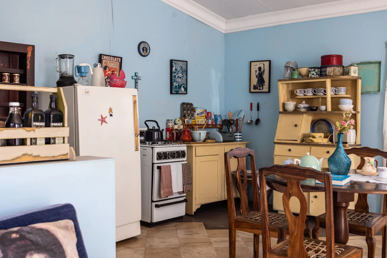 A kitchen with pale blue walls, yellow cupboards, a freestanding cooker and timber dining chairs.